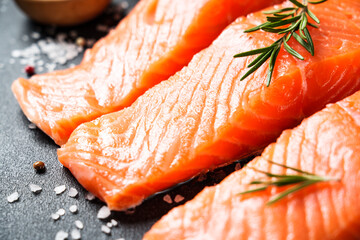 Salmon fillet, raw fresh fish with rosemary and spices at black background.