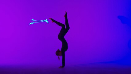 Female gymnast isolated on laser blue neon studio background. Girl dancer showing gymnastic elements on the floor.