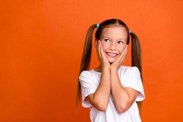 Photo portrait of pretty small girl touch cheeks admire look empty space dressed stylish white outfit isolated on orange color background