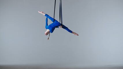 Female gymnast isolated on white studio background. Girl aerial dancer balancing spinning on gymnastic straps, showing dance elements
