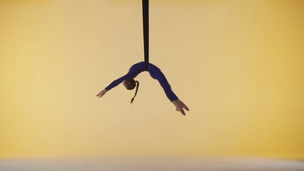 Female gymnast isolated on yellow studio background. Girl aerial dancer spinning on gymnastic straps, showing acrobatic elements.