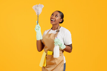 Happy african american woman cleaner dusting using feather duster, studio