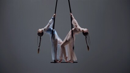 Female gymnastic duo isolated on monochrome studio background. Girls aerial dancers spin on...