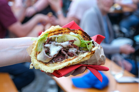 Nahaufnahme eines leckeren Pastramisandwiches mit Sauce und Gem&uuml;se in einer Kartoffelwaffel in der Hand einer Frau auf einem Fest, Konzert oder Streetfood-Festival drau&szlig;en, selektiver Fokus