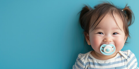 Smiling asian baby girl with pacifier portrait on flat blue background with copy space. Banner template with infant child smile.