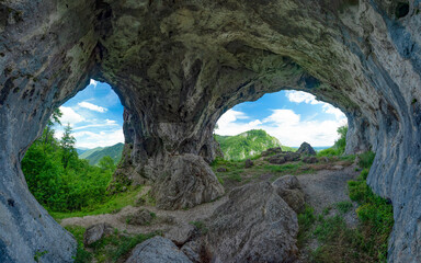 Viewpoint above mountains through a grotto, eroded in a calcareous cliff on a mountain side. The tunnel has its stone walls covered with moss. The arches in the cave resemble two eyes. Carpathia - Powered by Adobe