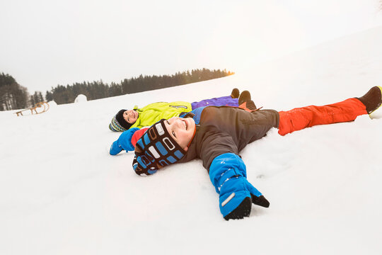 Two boys making snow angels and playing in the snow in winter. Wolfratshausen, Bavaria, Germany 