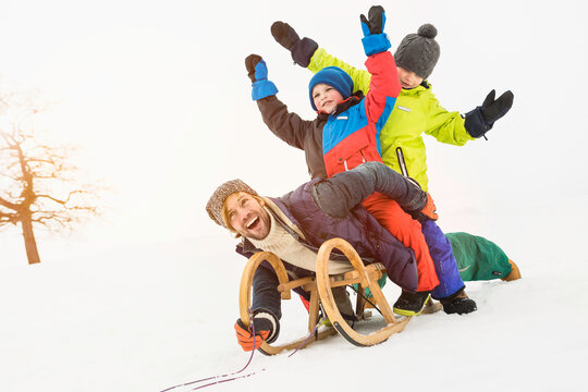 Two boys playing in the snow and sledding with their father in winter. Wolfratshausen, Bavaria, Germany 