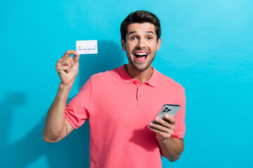 Portrait of emotional business developer guy use smartphone speechless use credit card to buy gifts isolated on cyan color background
