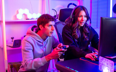 Couple or friends have shocking, exciting face with fun, using joystick to compete and play games together, sitting in room at home with neon decorated light. Game online streamer Concept.