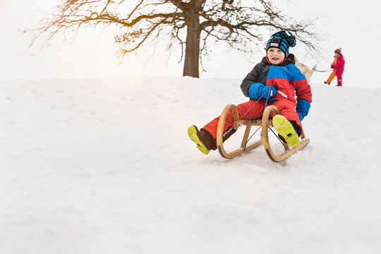 Two young boys sledding down a hill in winter. Wolfratshausen, Bavaria, Germany 