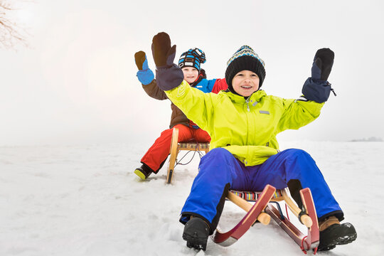 Two young boys sledding down a hill in winter. Wolfratshausen, Bavaria, Germany 