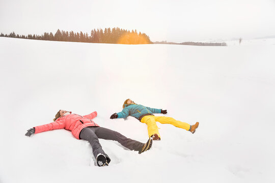 Couple making snow angels in the snow in the winter. Wolfratshausen, Bavaria, Germany