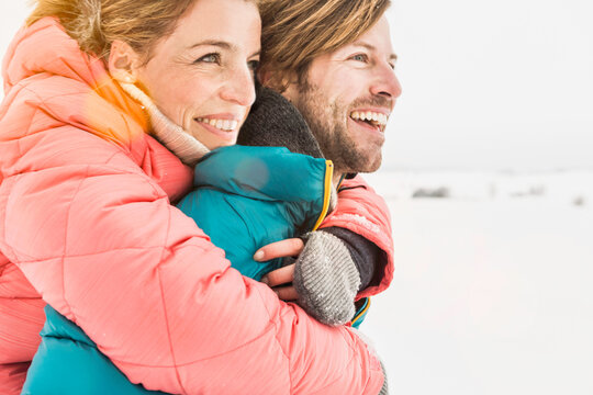 Man carries his wife piggy back across a field in the snow in winter. Wolfratshausen, Bavaria, Germany