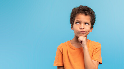 Thoughtful boy in orange, pondering on blue background, free space