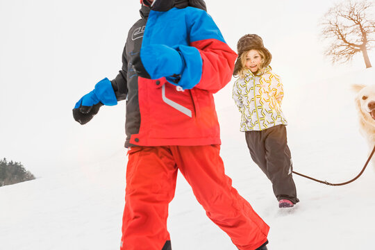 Two kids and a dog running through the snow and playing. Wolfratshausen, Germany