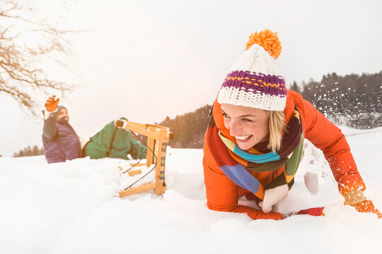 Young couple lying in the snow after crashing while sledding down a snowy hill in the winter. Wolfratshausen, Bavaria, Germany