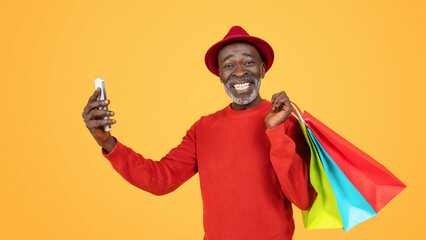 An ecstatic senior man in a red outfit and hat, taking a selfie with his phone