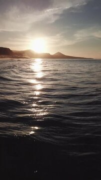 Sunset on the beaches of Gran Canaria, flying near the water, while recording waves and an epic sky, vertical video recorded with drone in 4k