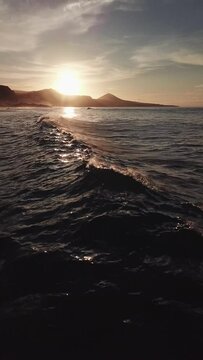 Sunset on the beaches of Gran Canaria, flying near the water, while recording waves and an epic sky, vertical video recorded with drone in 4k
