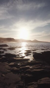 Sunset on the beaches of Gran Canaria, flying near the water, while recording waves and an epic sky, vertical video recorded with drone in 4k