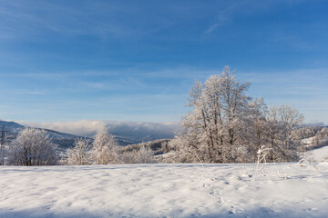 Fantastic winter landscape with wooden house in snowy mountains. Hight mountain peaks in foggy sunset sky. Christmas and winter vacations holiday concept