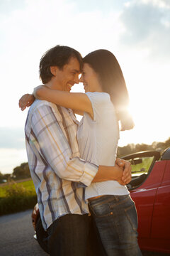 young couple  hugging in front of an electric car