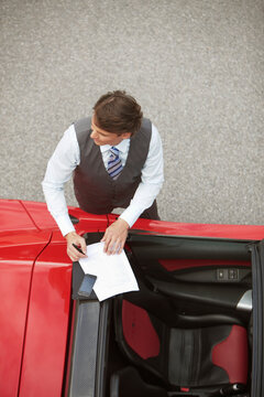 Top shot of man in business attire standing next to electric sports car signing documents. Munich, Bavaria, Germany