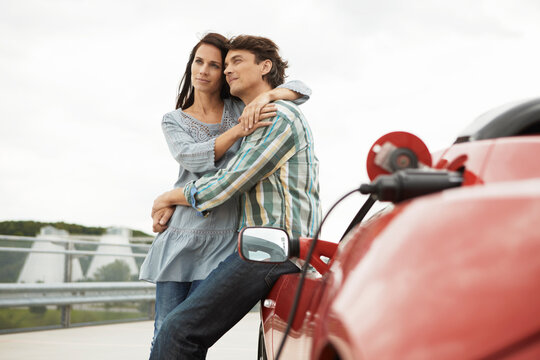 Couple hanging out on a roof top car park with electric car in foreground. Munich, Bavaria, Germany