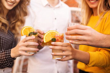 Crop happy friends drinking cocktails together