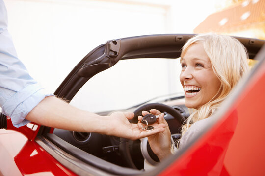Woman being given the keys for her new red convertible electric sports car in front of modern house and garage. Munich, Bavaria, Germany