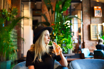 Attractive cute caucasian girl in black tshirt and black hat drinkig cold citrus juice or lemonade