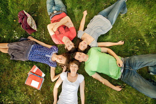 Group of young students taking break from learning together while in a park, laying on their backs and looking up at the clouds.