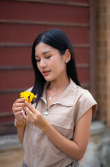 A young woman in a vintage dress holds a yellow flower and looks at it to admire the flowers in her hand.