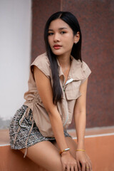 A young woman dressed in vintage clothing sits by a wall and looks back at the camera.