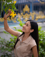 A teenage girl wearing a vintage dress reached out with her left hand and grabbed a flower on a tree, admiring its beauty.