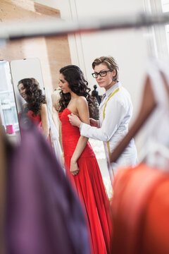 Beautiful dark skinned woman is being fitted in an evening gown by fashion designer and his 3 tailors. Munich, Bavaria, Germany