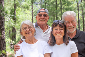 Joyful group of senior friends enjoying retirement trekking in the forest, four elderly people looking at camera smiling. Sport, freedom, healthy lifestyle concept