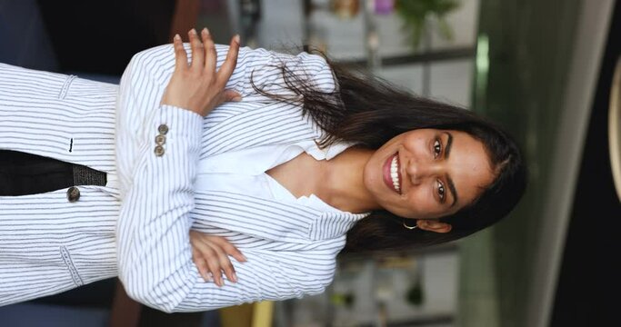 Happy Indian businesswoman in formal wear posing with arms crossed in modern office, vertical shot. Beautiful young female worker, executive manager portrait. Business, promotion, professional success
