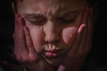 Cute little sad offended child girl is crying on a black background. Close up portrait.