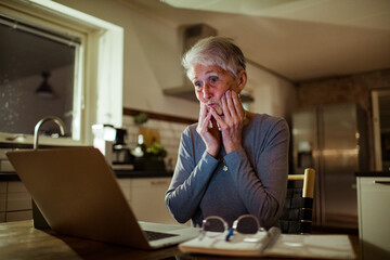 Senior Woman Working on Finances with Laptop and Papers in Kitchen at Night