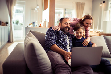Happy family with child using laptop on couch at home