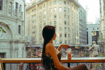 Fototapeta na wymiar young woman sitting in a store with a juice looking out the window at the city. copy space