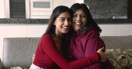 Young 20s daughter her 50s mom embracing sit on couch smile look at camera, showing bond, feeling love, spend priceless time together celebrate Happy Mother Day, appreciate their strong family ties