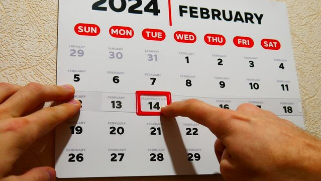 Close-up of a beautiful February page of the wall calendar 2024 and a male hand moves a red cursor to the Valentine's Day date