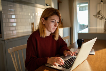Woman typing on laptop in home kitchen