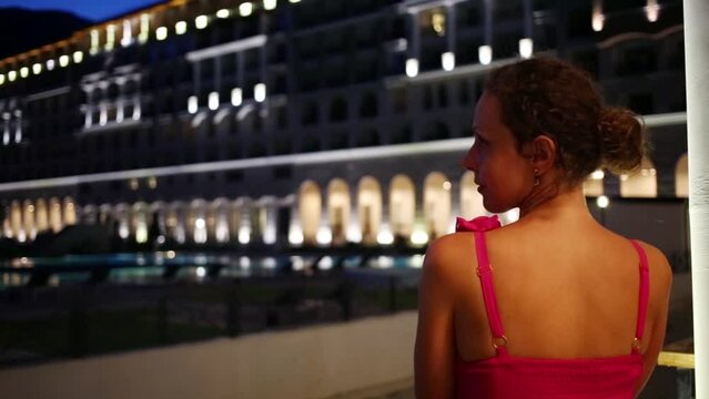 Back of woman in pink dress looking at building with illumination