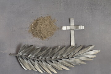 Ash, silver cross and silver palm leaf on grey background. Ash Wednesday concept.
