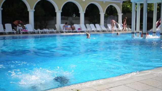Boy and girl dive together to pool with Jacuzzi, sun loungers