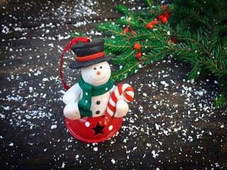 Snowman ornament and Christmas tree branch placed on a rustic wooden table decorated with fake snow